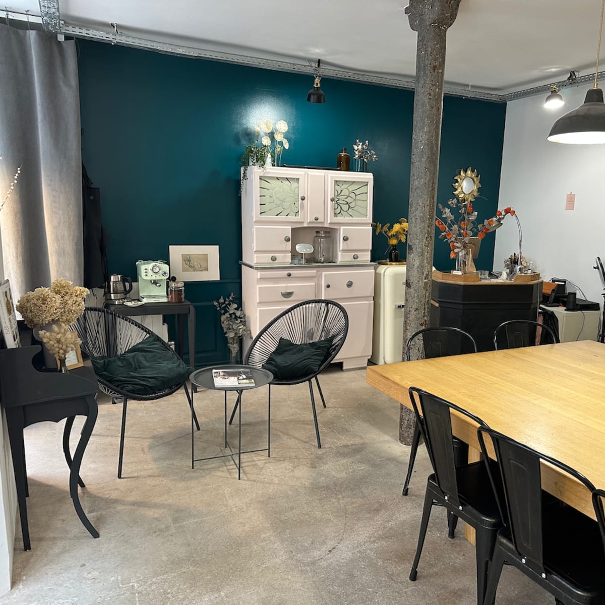 A cozy interior space features a wooden dining table, black chairs, and a mix of decorative items against a teal wall.