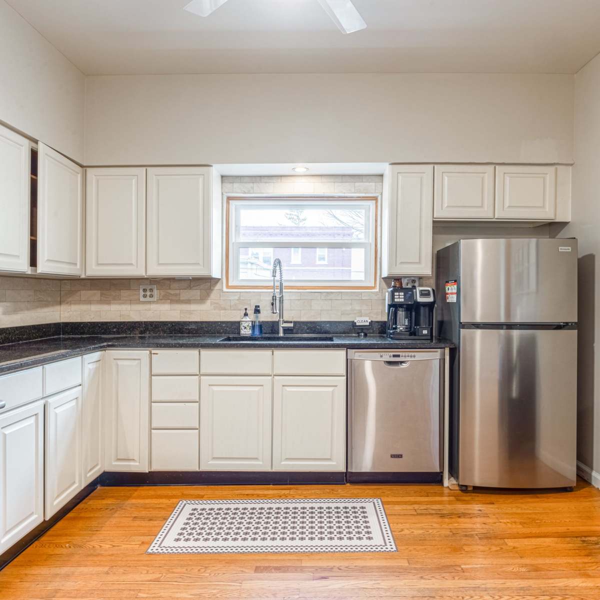 A modern kitchen with white cabinets, stainless steel appliances, and hardwood flooring.