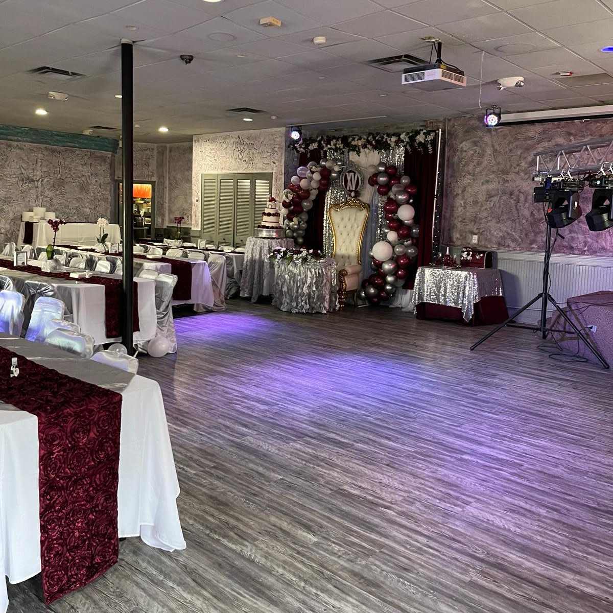 A decorated event space with tables set up and a backdrop featuring balloons and a cake display.