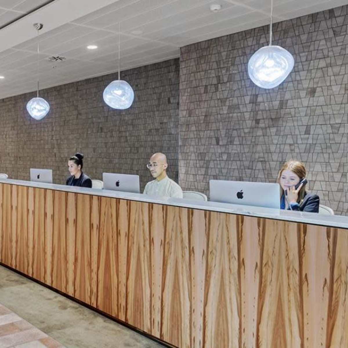 A modern reception area with a wooden front desk and three staff members working on computers under pendant lighting.