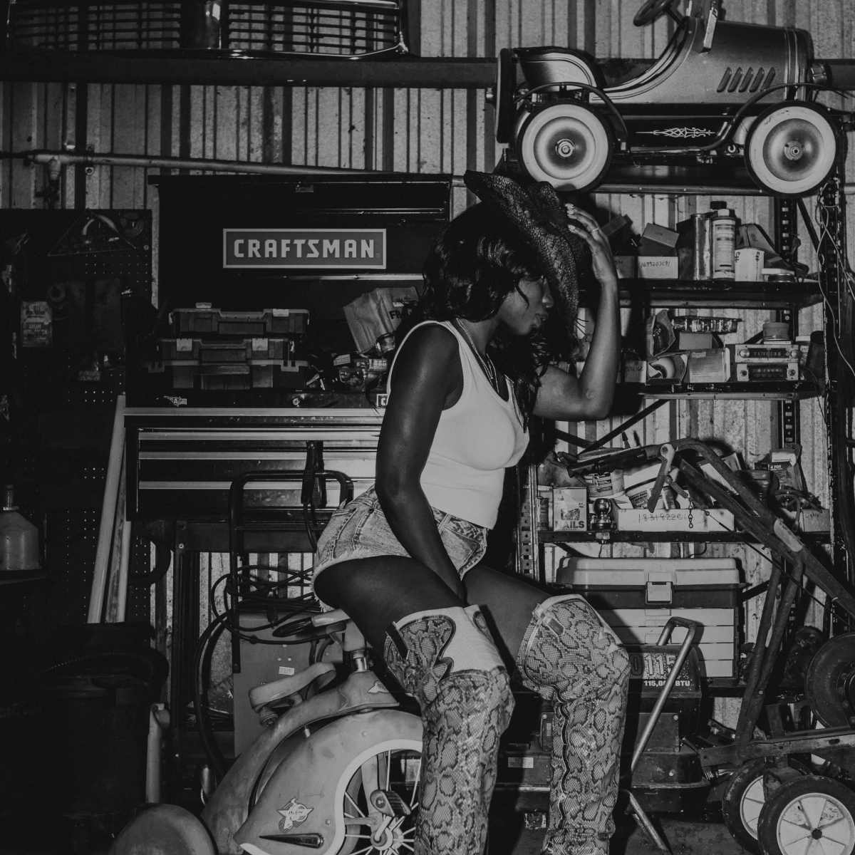 A person sits on a small toy vehicle in a garage filled with tools and equipment.