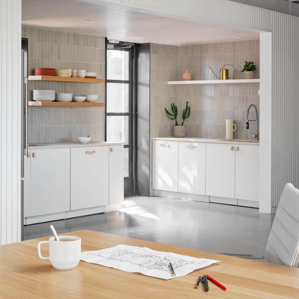 A modern kitchen features white cabinetry, open shelves displaying dishware, and a dining table with a sketch on it.