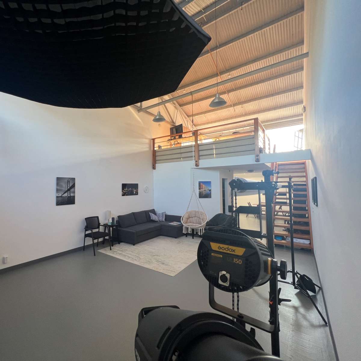 A spacious, well-lit studio featuring a couch, a rug, a small table, a staircase, and various photography equipment.