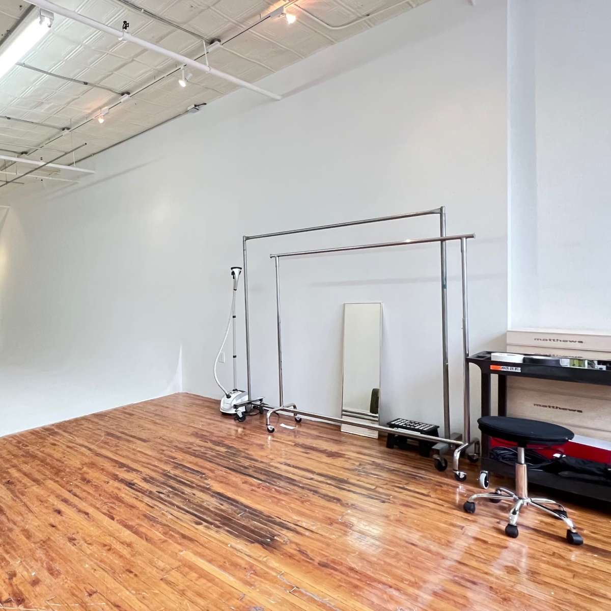 A spacious, empty studio with white walls, a smooth white backdrop, polished wooden floors, and a mirror on a silver stand.
