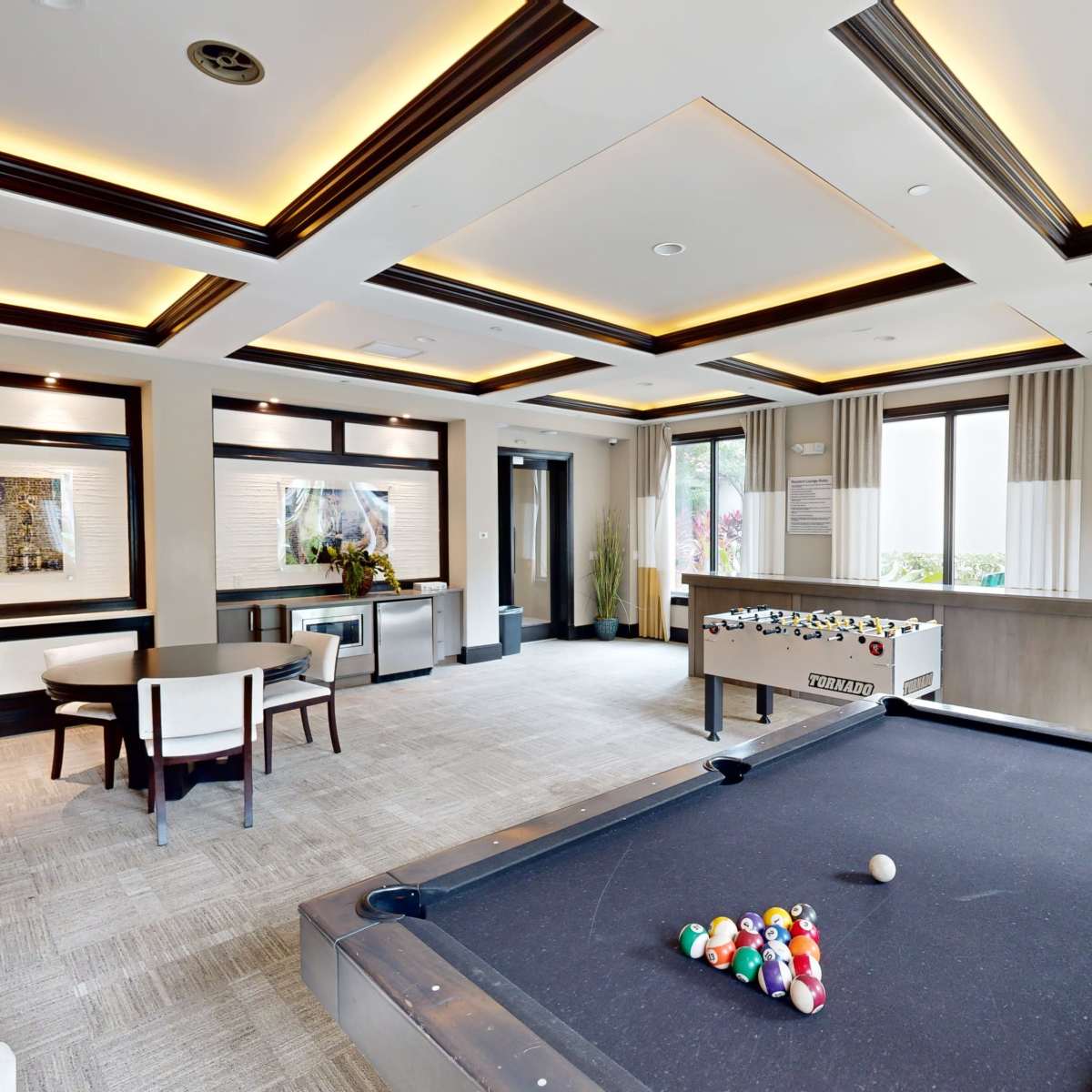 A well-lit recreational room featuring a pool table, foosball table, and modern seating arrangements.