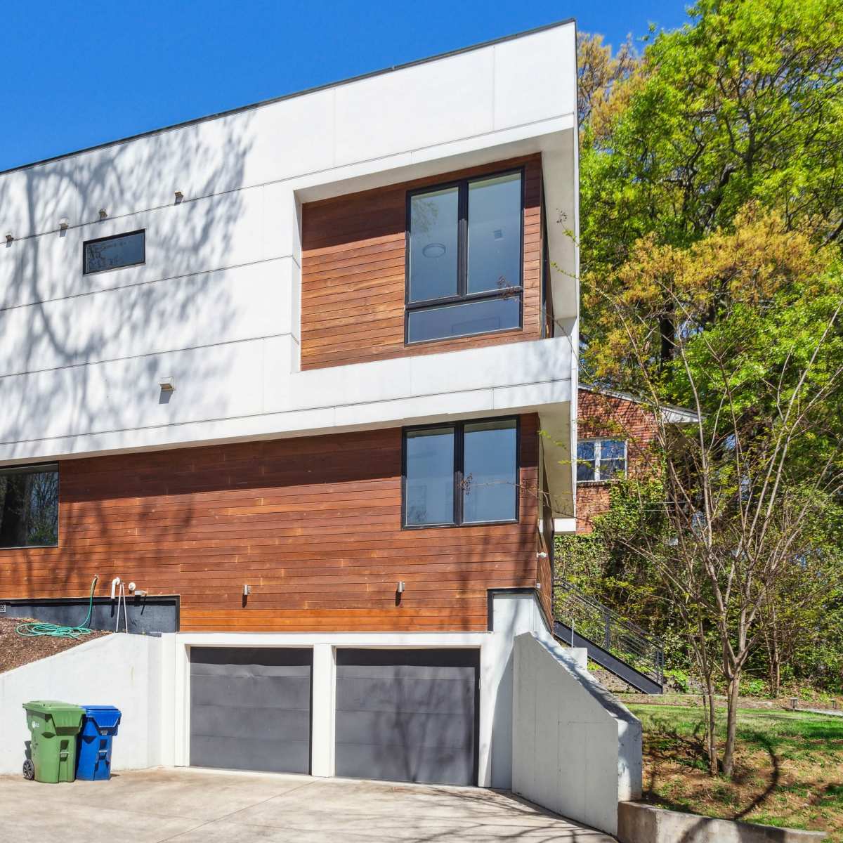 A contemporary two-story house with a mix of wooden and white exterior walls, featuring large windows and a garage below.