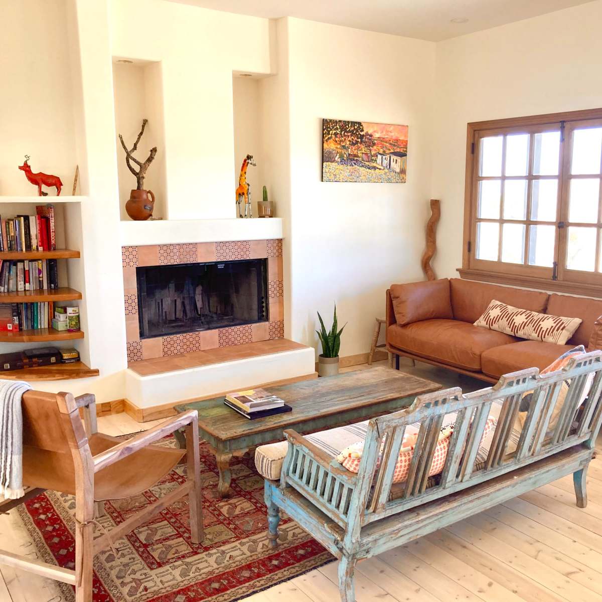A well-lit living room with a fireplace, a wooden coffee table, two leather sofas, and a bookshelf filled with books.