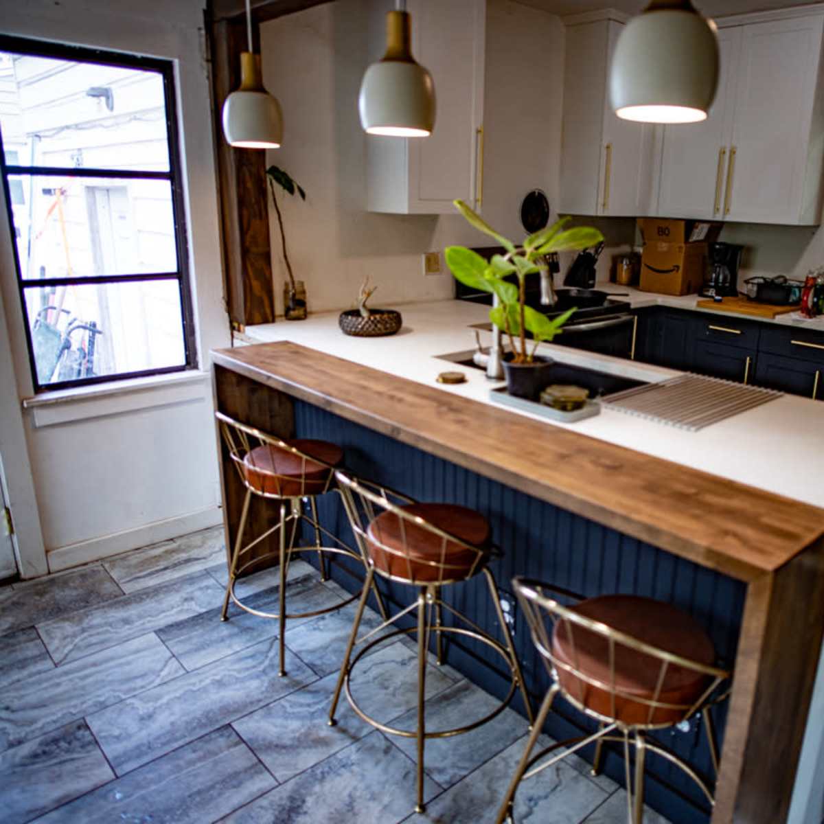 A modern kitchen with a central island featuring three bar stools, surrounded by cabinets and appliances.