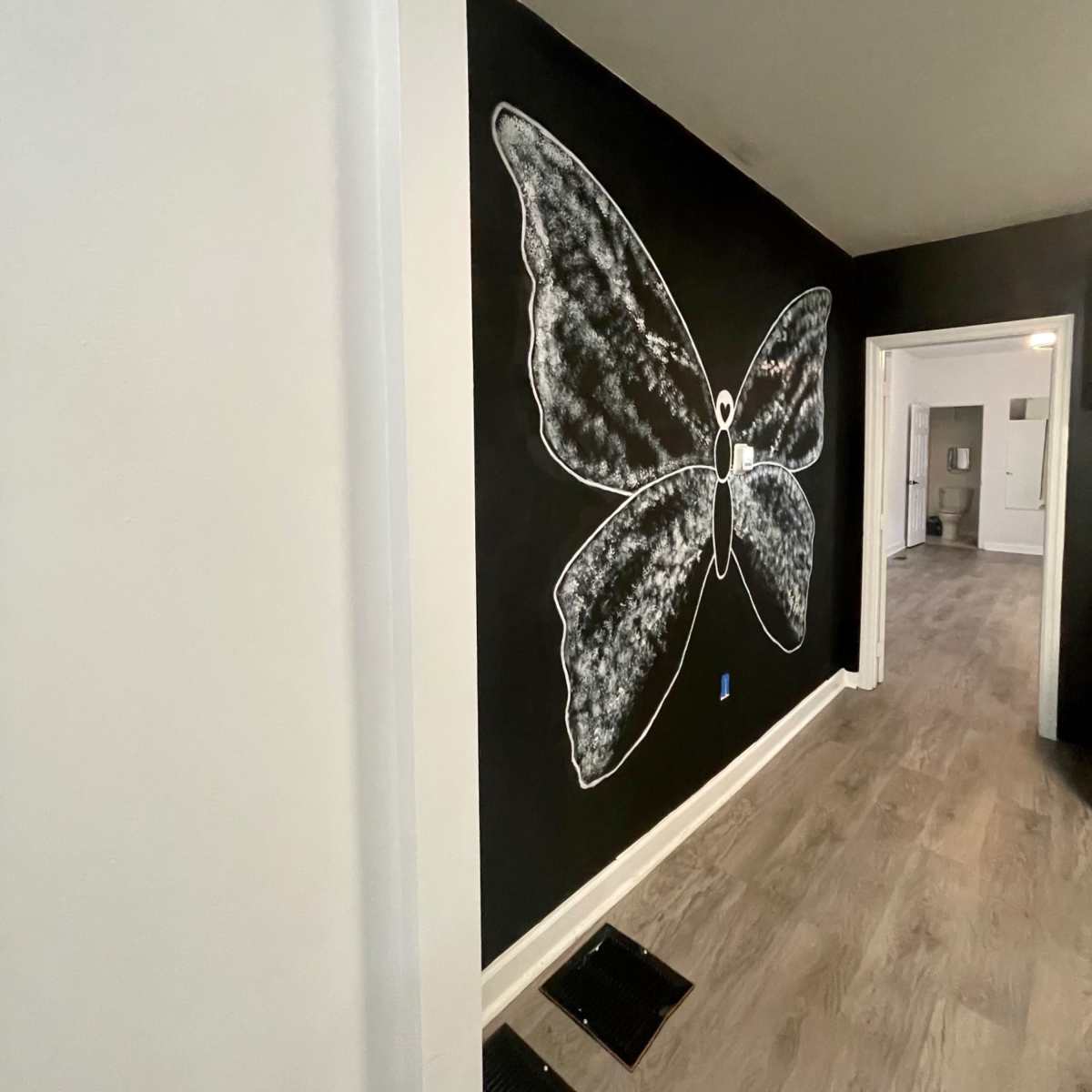 A large butterfly mural is painted in white chalk on a black wall in a hallway.