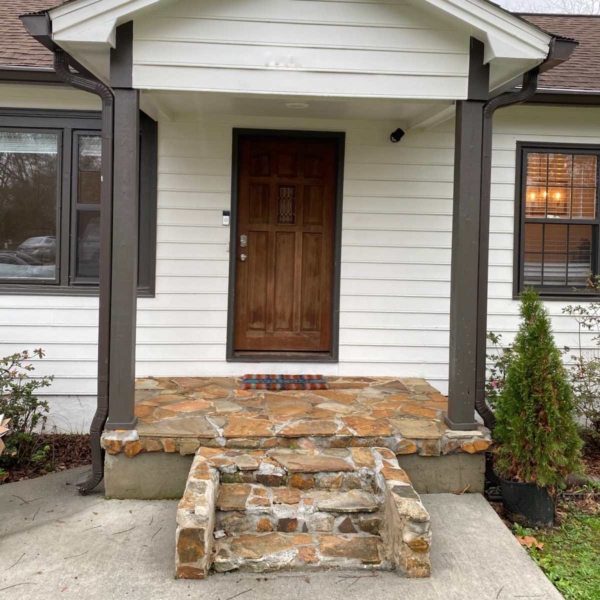 The front entrance of a house with a wooden door, stone steps, and a porch framed by dark columns.