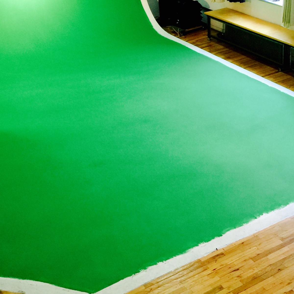 A large green backdrop is set up in a room with wooden floors and windows, while a person stands nearby.