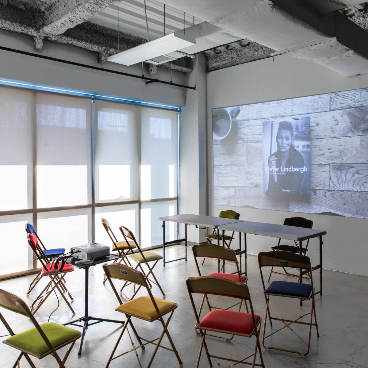 A projector displays an image on a wall in a room set up with rows of colorful chairs and a long table.