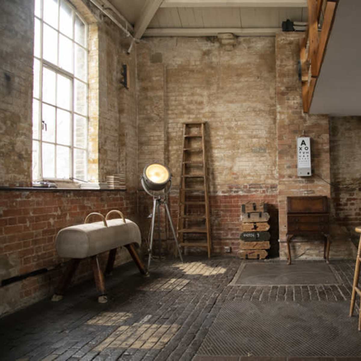 A spacious, industrial-style room with exposed brick walls, wooden furniture, and a large window allowing natural light to enter.