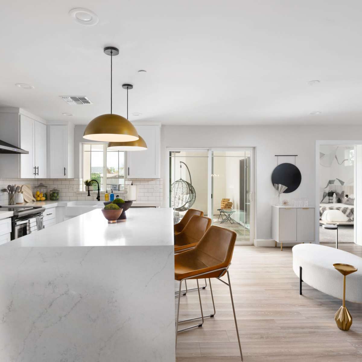 A modern kitchen features white cabinetry, a large marble island with bar stools, and an open layout connecting to a dining area.
