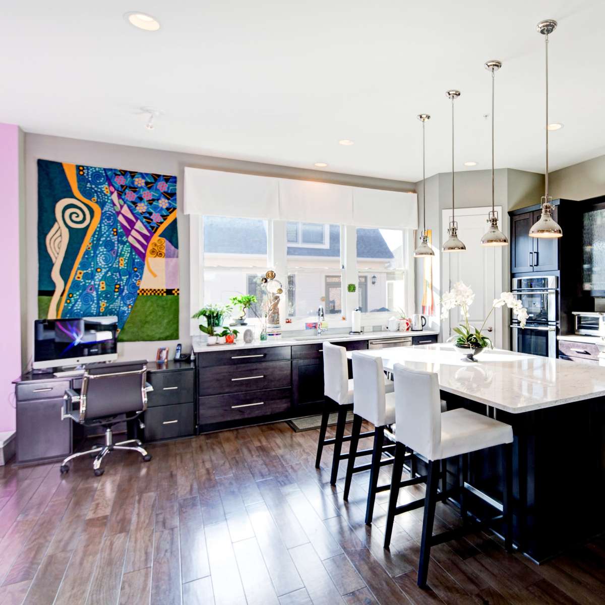 A modern kitchen featuring a central island with bar stools, dark cabinetry, and stainless steel appliances, illuminated by pendant lights.