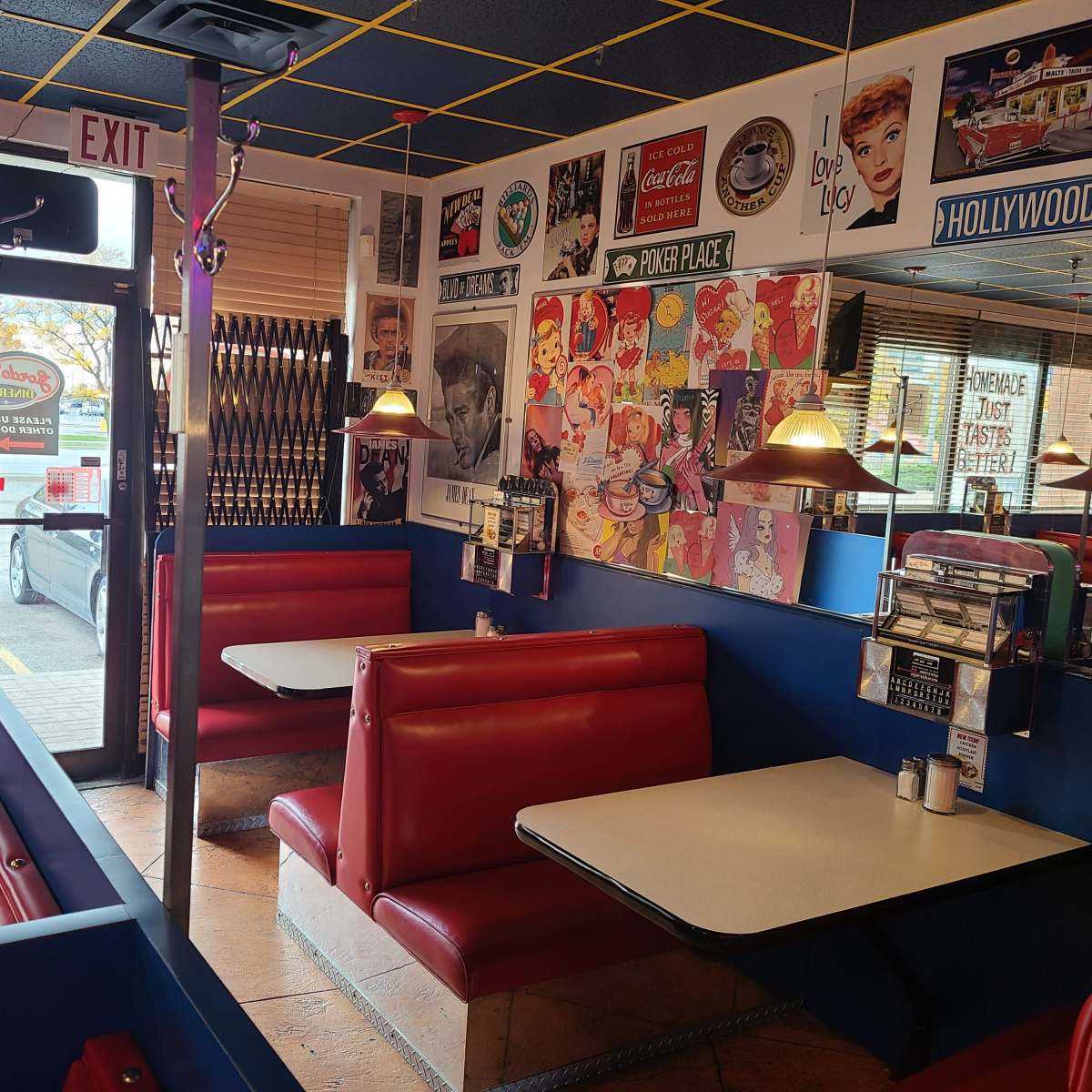 The interior of a diner featuring red vinyl booths, a table in the center, and vintage advertisements on the walls.