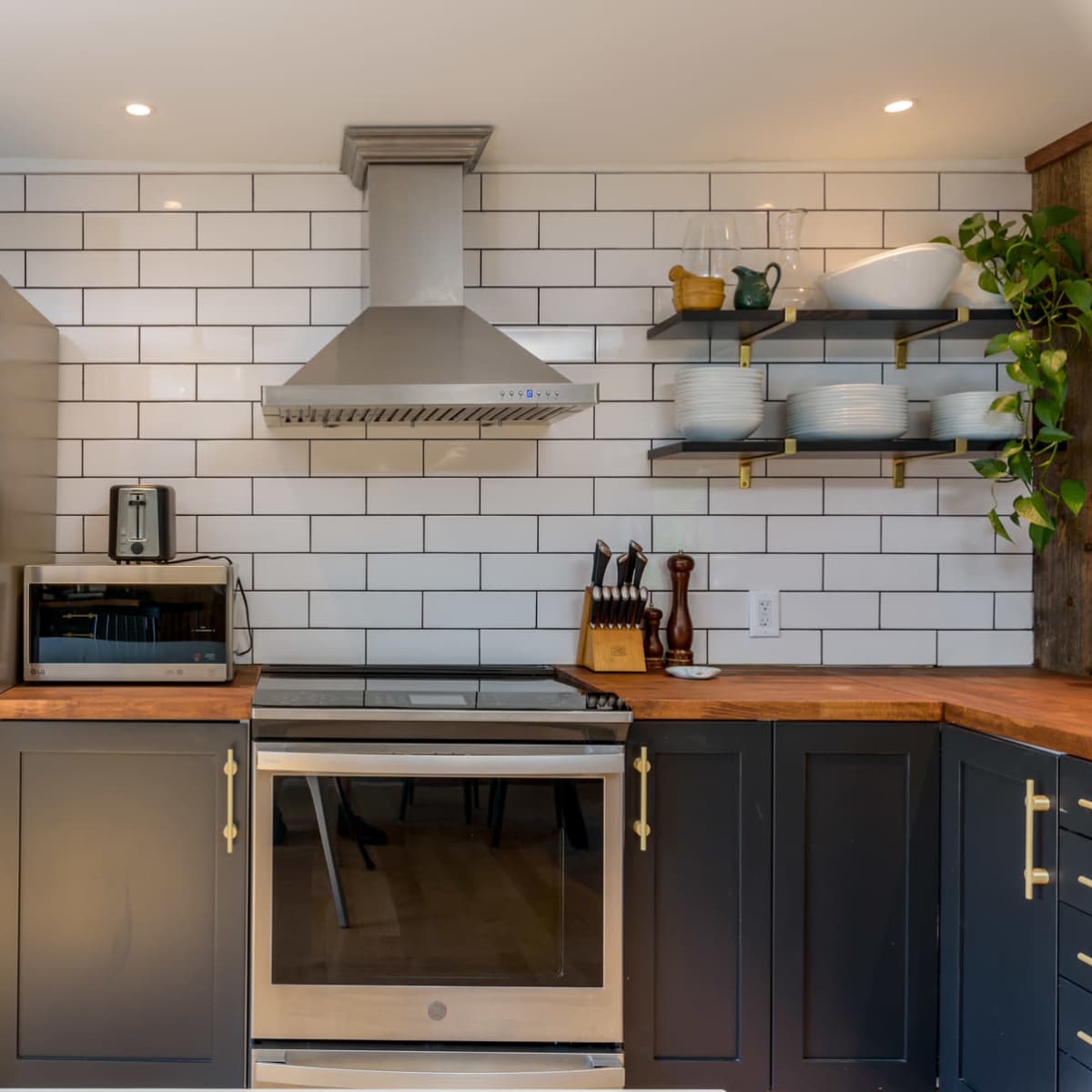 A modern kitchen featuring stainless steel appliances, a tiled backsplash, and dark cabinetry with wooden countertops.