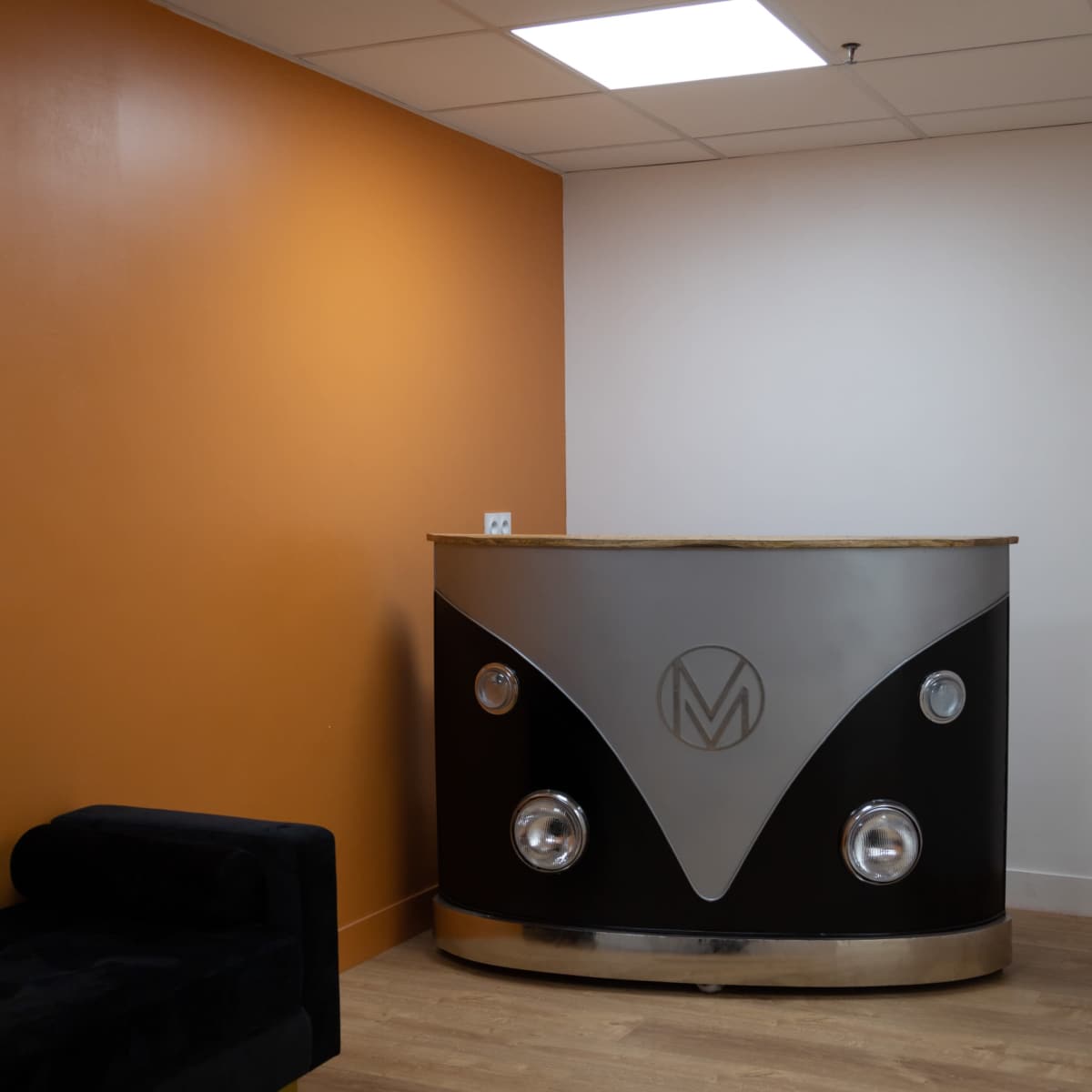 A reception desk with a metallic front and an orange wall behind it in a modern office space.