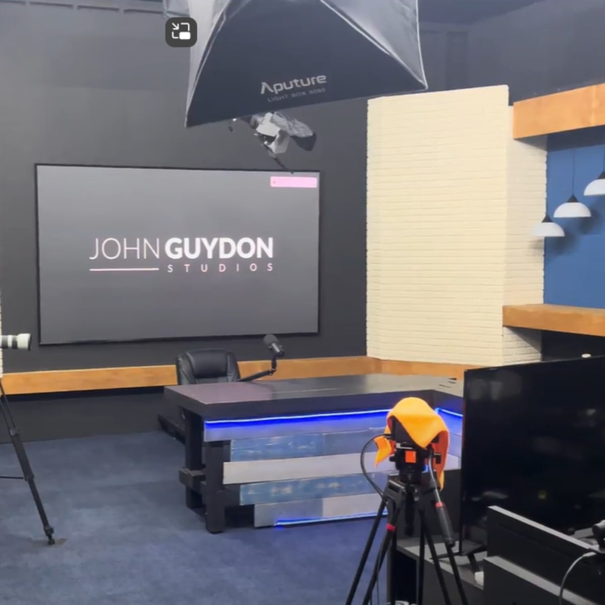 A video studio set up with cameras, lighting equipment, and a central desk featuring a backdrop that reads "JOHN GUYDON STUDIOS."
