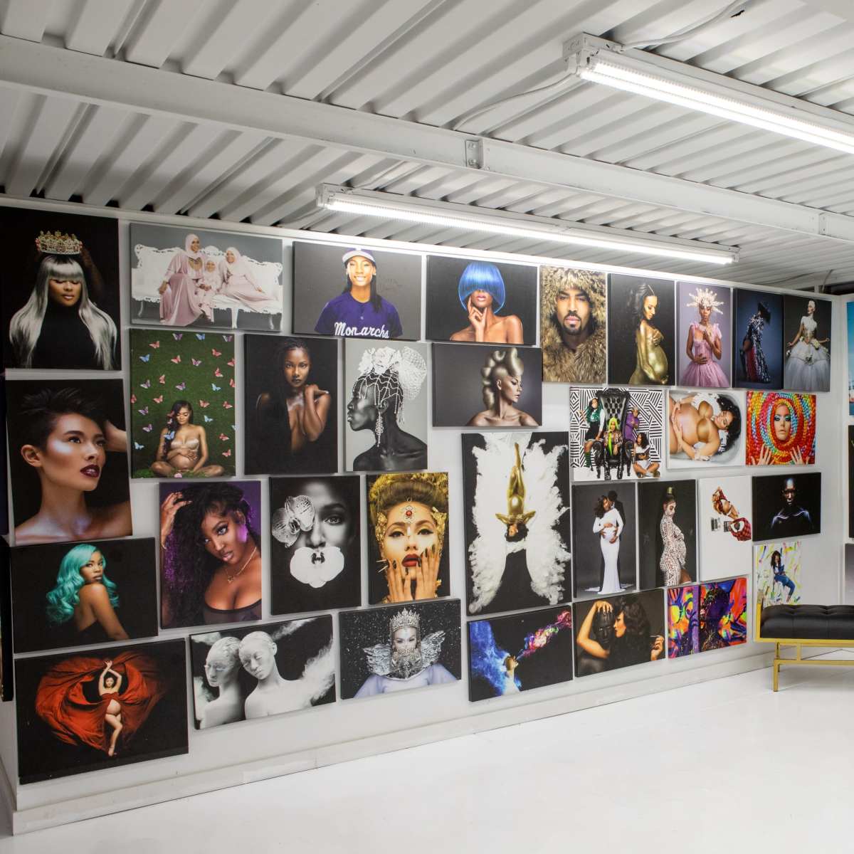 A gallery space with a white floor and walls adorned with various large photographs and artworks, featuring portraits of diverse individuals and artistic compositions.