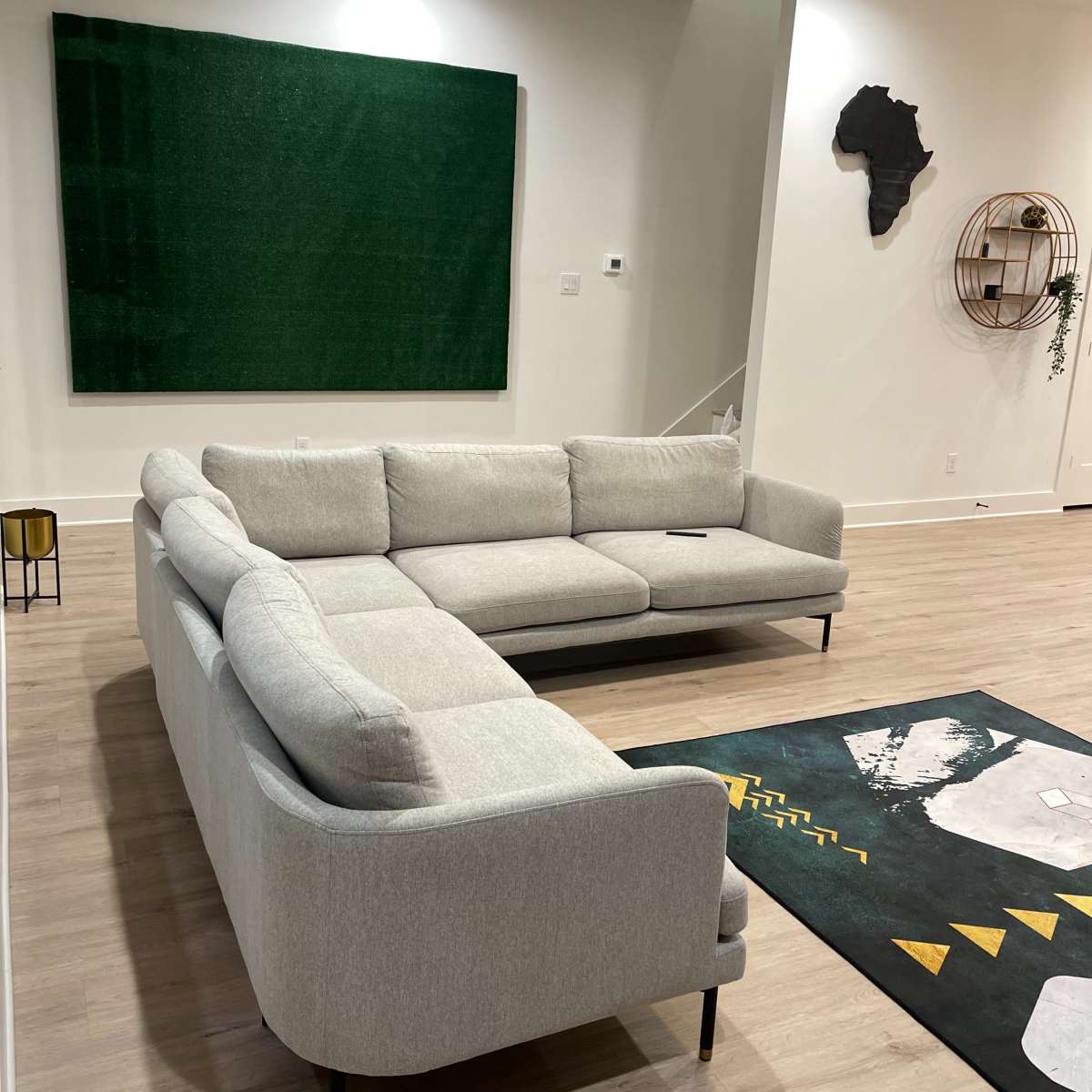 A sectional gray sofa is positioned in a modern living room with wooden flooring and a green accent wall featuring a decorative map of Africa.