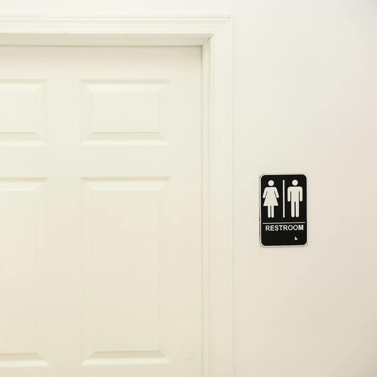 A closed white door with a sign indicating the location of a restroom.