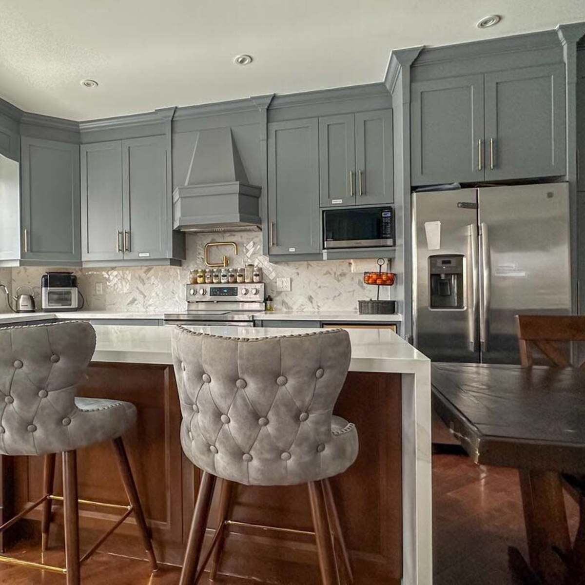 A modern kitchen features gray cabinetry, a white countertop, and two upholstered bar stools at a central island.
