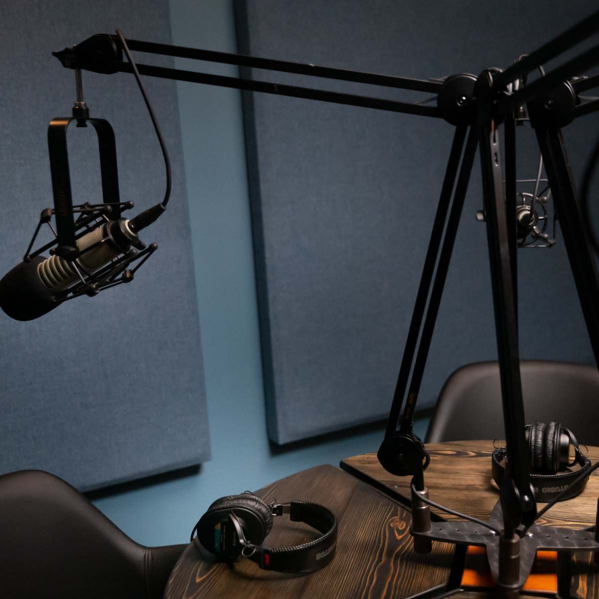 A podcast recording setup with two microphones on adjustable arms and headphones placed on a wooden table, surrounded by soundproofing panels.