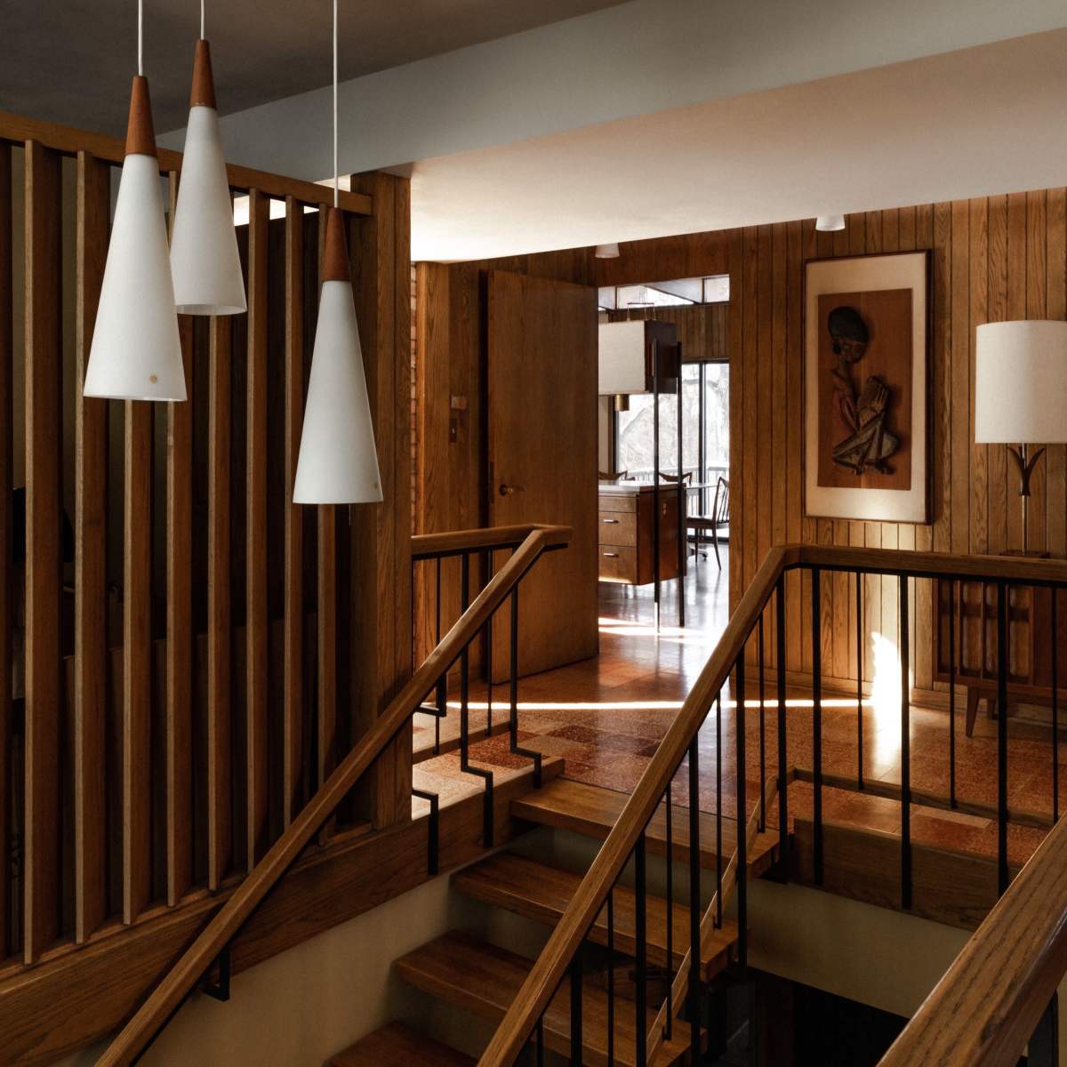 A modern staircase with wooden railings leads to an upstairs area, featuring a pendant light and a wooden wall with artwork.