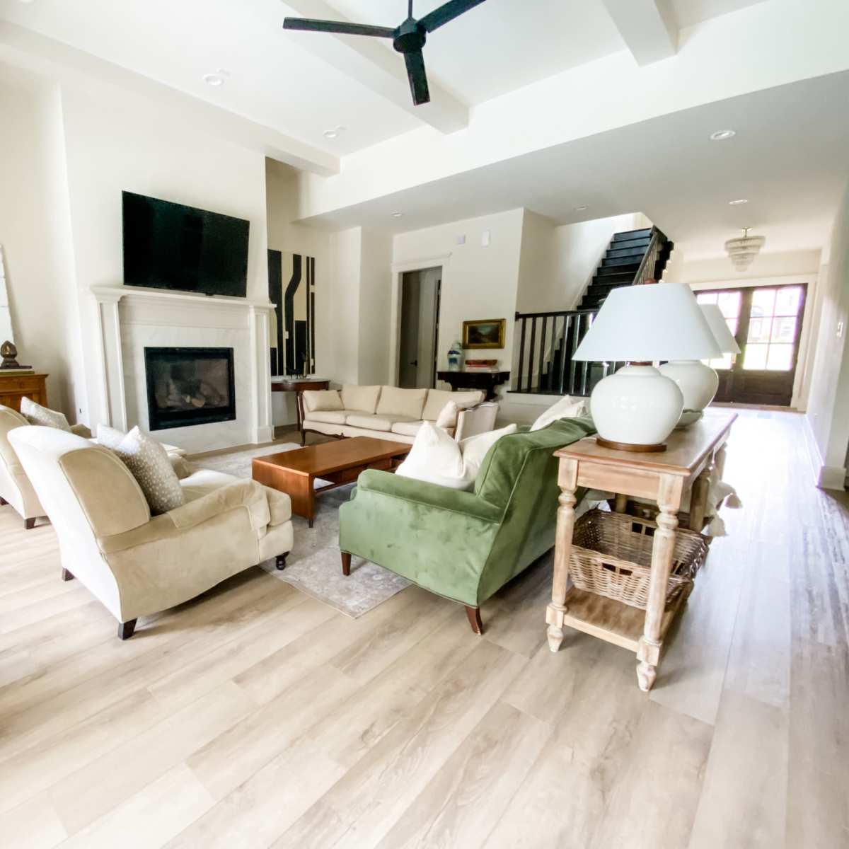 A spacious living room features a fireplace, TV, and various seating arrangements, complemented by neutral-colored walls and wooden flooring.