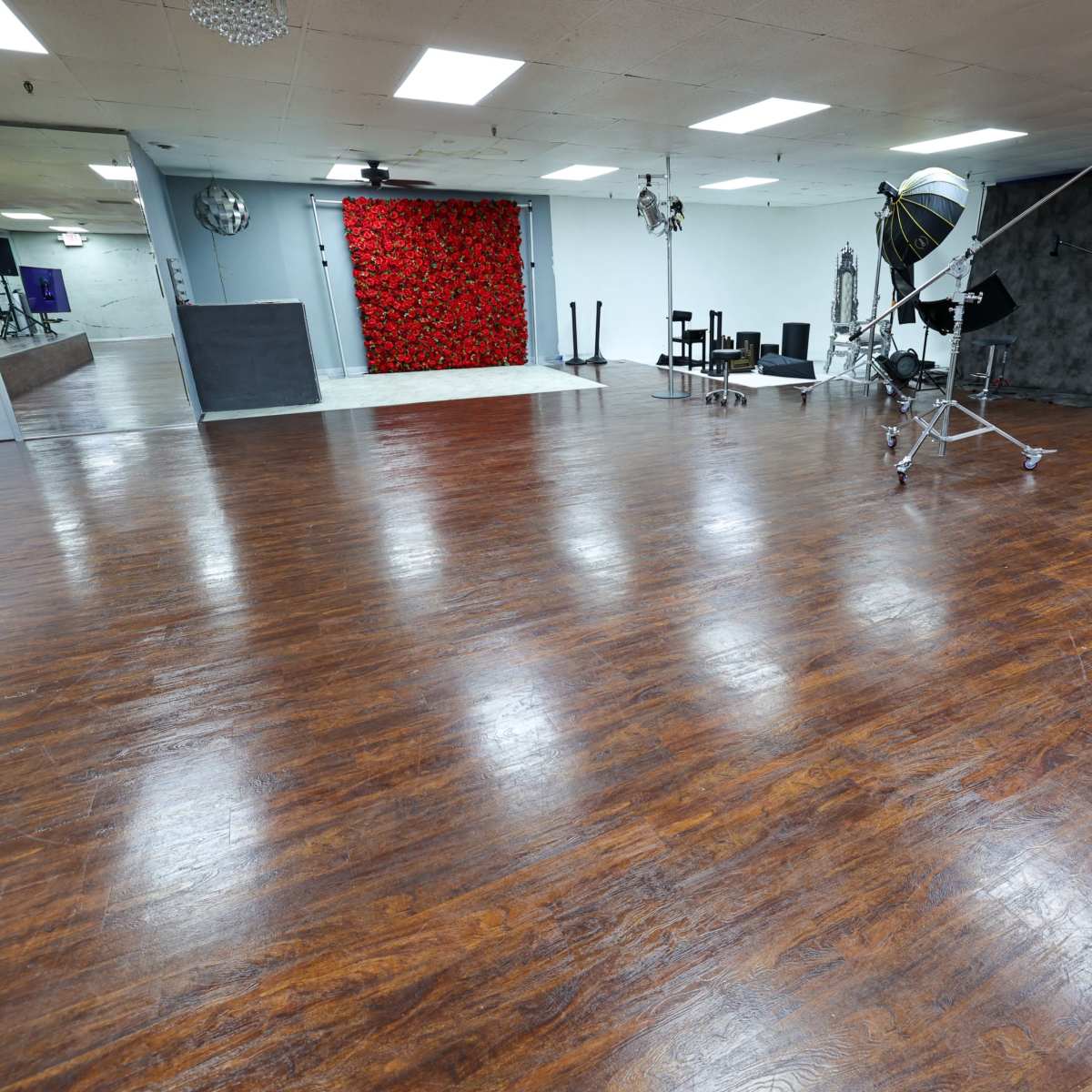 A spacious studio with a polished wooden floor, featuring a red floral backdrop and various photography equipment set up in the background.