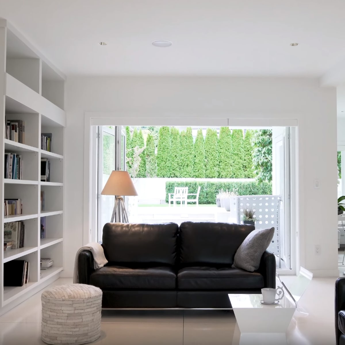 A modern living room with a black sofa, a white bookcase, and large windows leading to a patio.