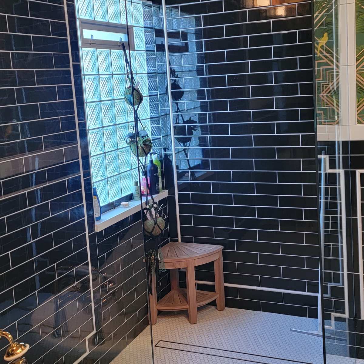 A modern bathroom with a glass shower enclosure, black tile walls, and a freestanding bathtub on a patterned floor.