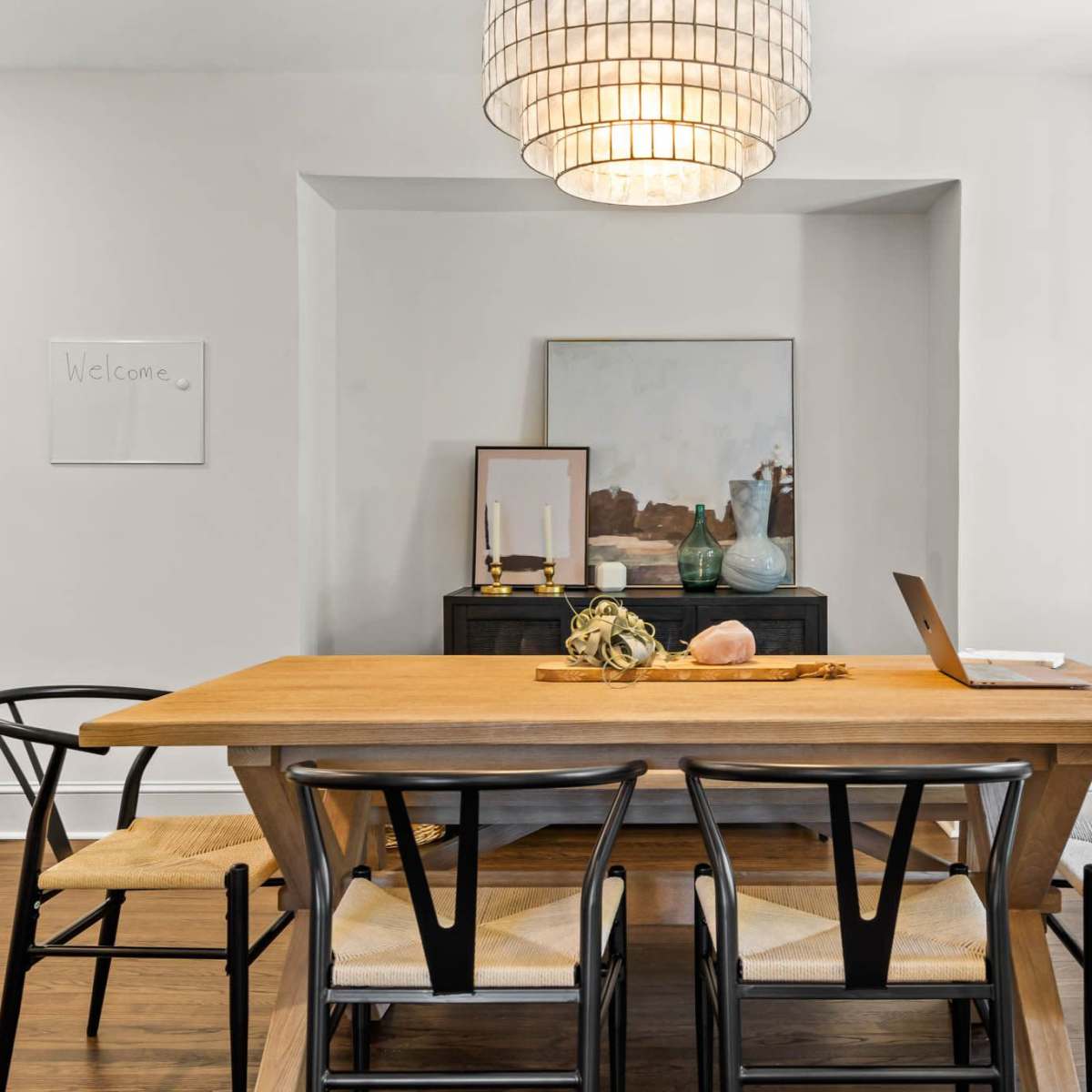 A dining room features a wooden table surrounded by black chairs, with a large pendant light overhead and decorative items on a sideboard.