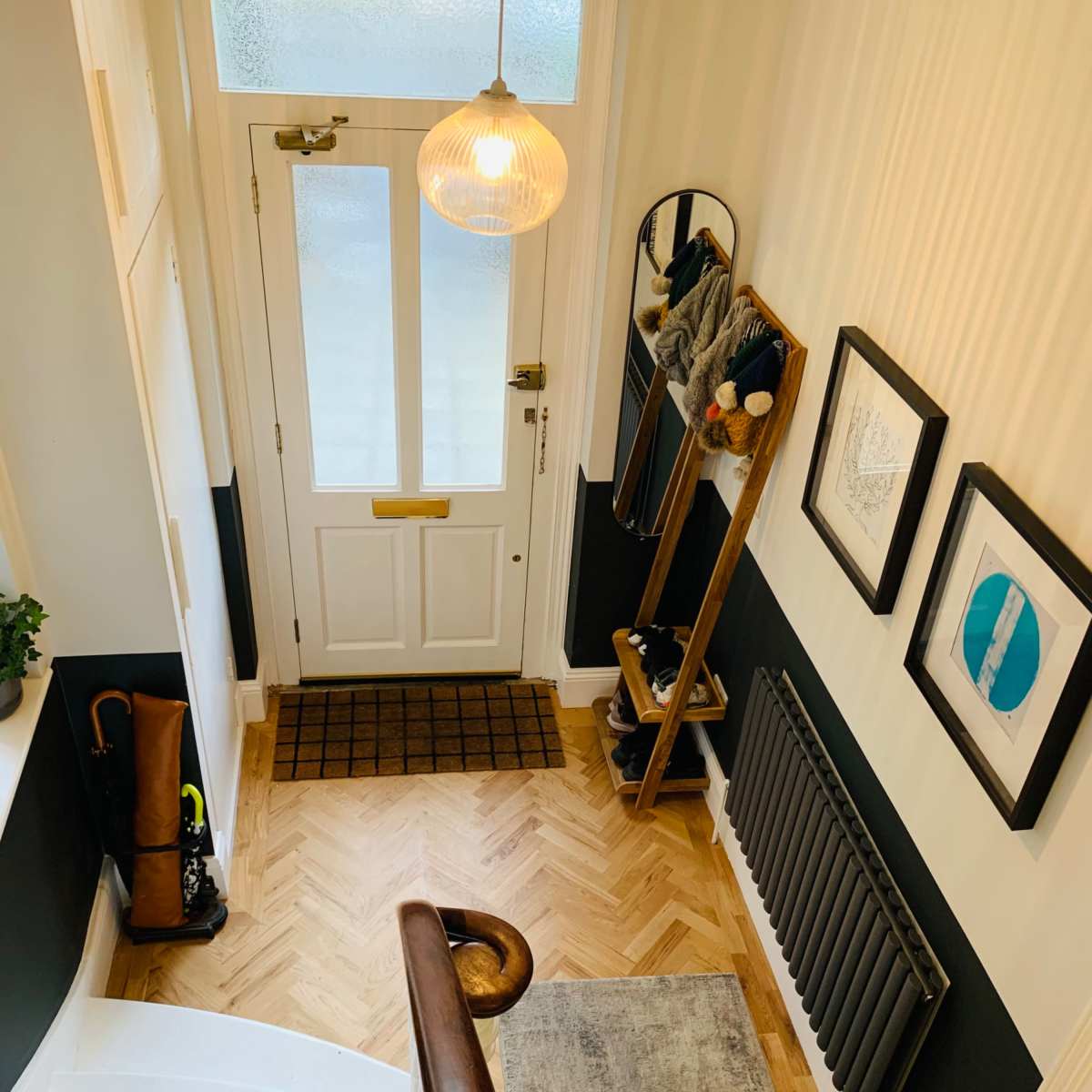 A staircase leading to a hallway with a wooden front door, a coat rack, framed artwork, and a radiator.