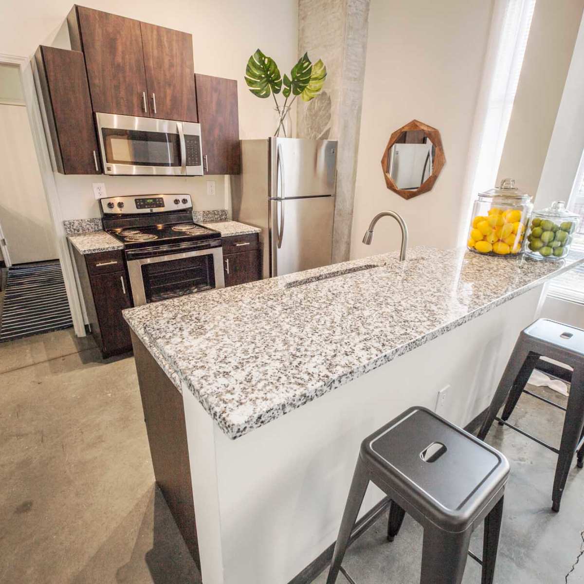 A modern kitchen features granite countertops, stainless steel appliances, and bar stools beside a window with natural light.
