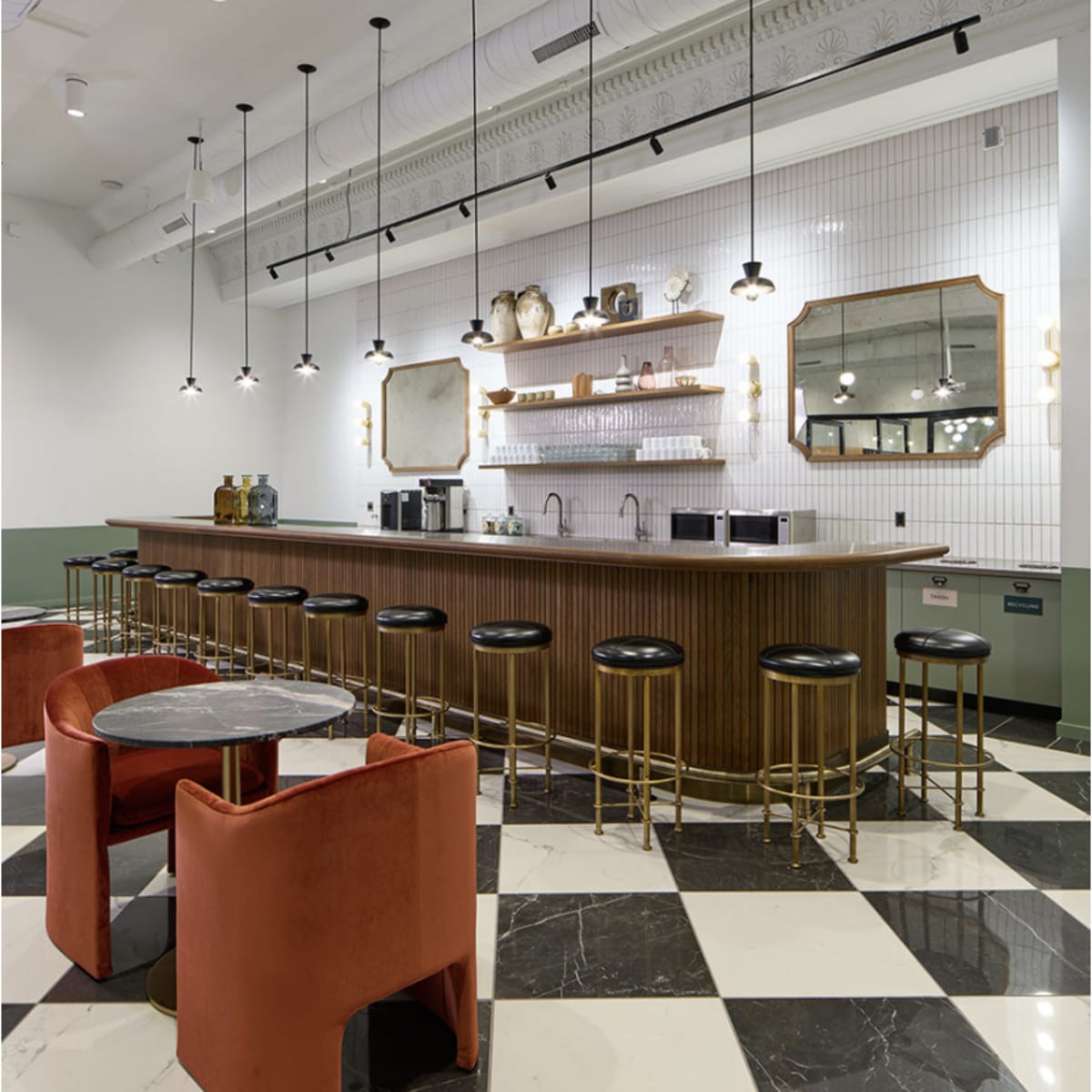A modern café with a wooden bar, black stools, and pendant lights, featuring a patterned floor of black and white tiles.