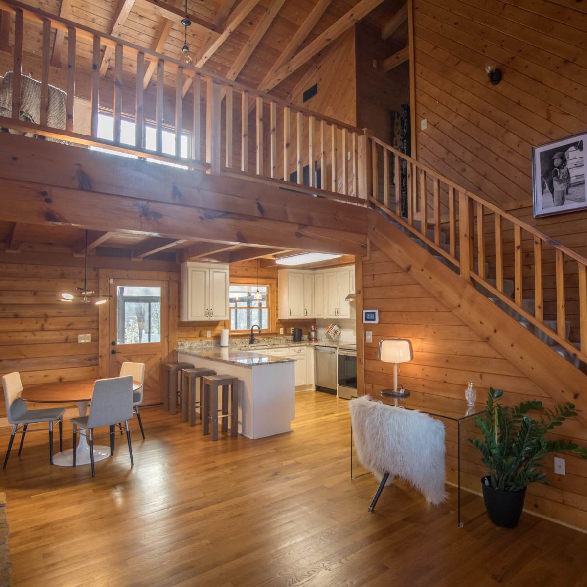 A wooden interior of a cabin featuring a staircase, a dining area with a table, and a kitchen area with an island.