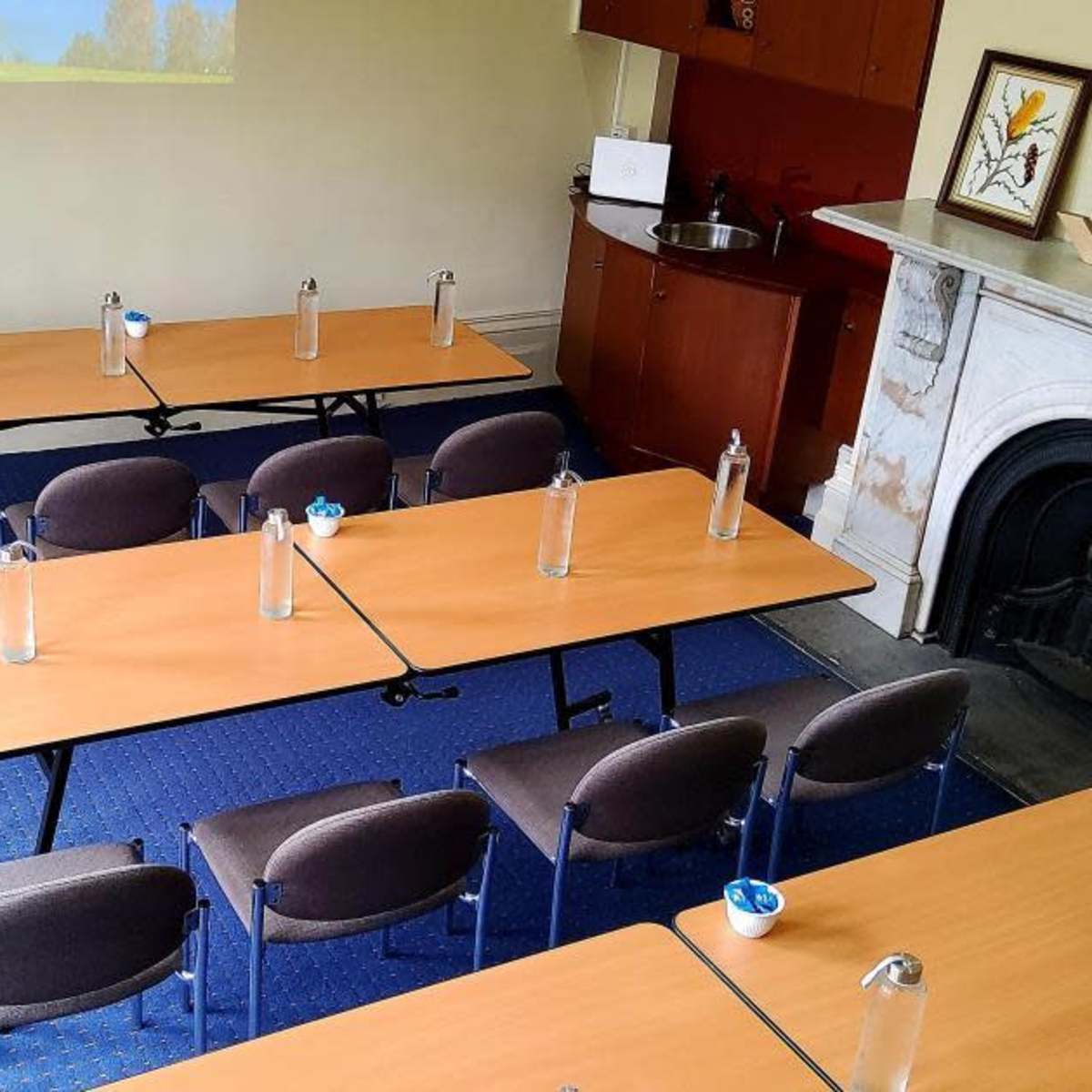 A meeting room features several tables arranged in a U-shape, each with a water bottle, and chairs lined up around them.