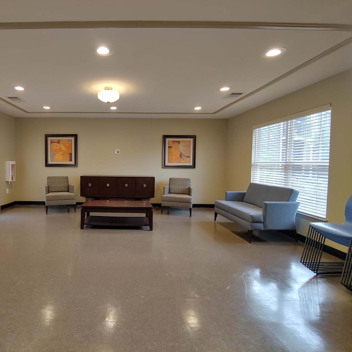 A spacious, well-lit room with two chairs, a sofa, a coffee table, and artwork on the walls, along with large windows allowing natural light in.