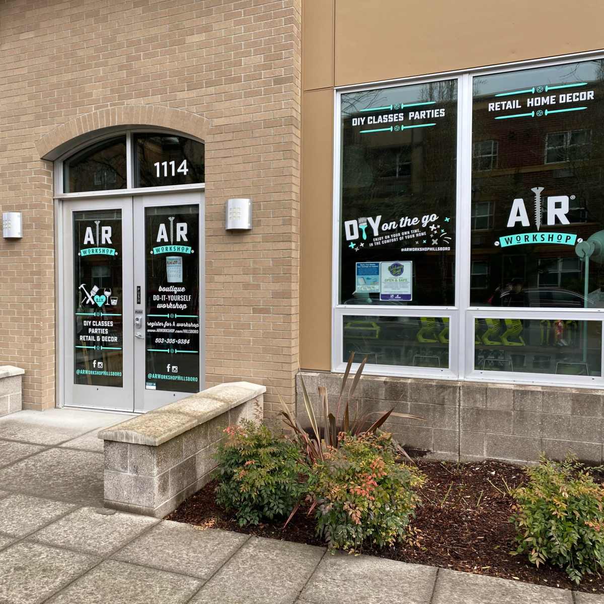 A storefront with large glass doors and windows displaying the business name "AR Workshop" along with promotional graphics for DIY classes and home decor.