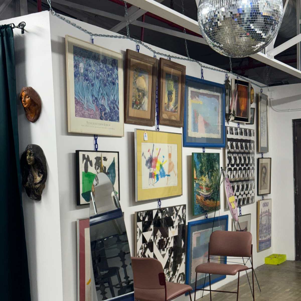 A wall adorned with various framed artworks and photographs, complemented by two modern chairs and a large disco ball hanging from the ceiling.