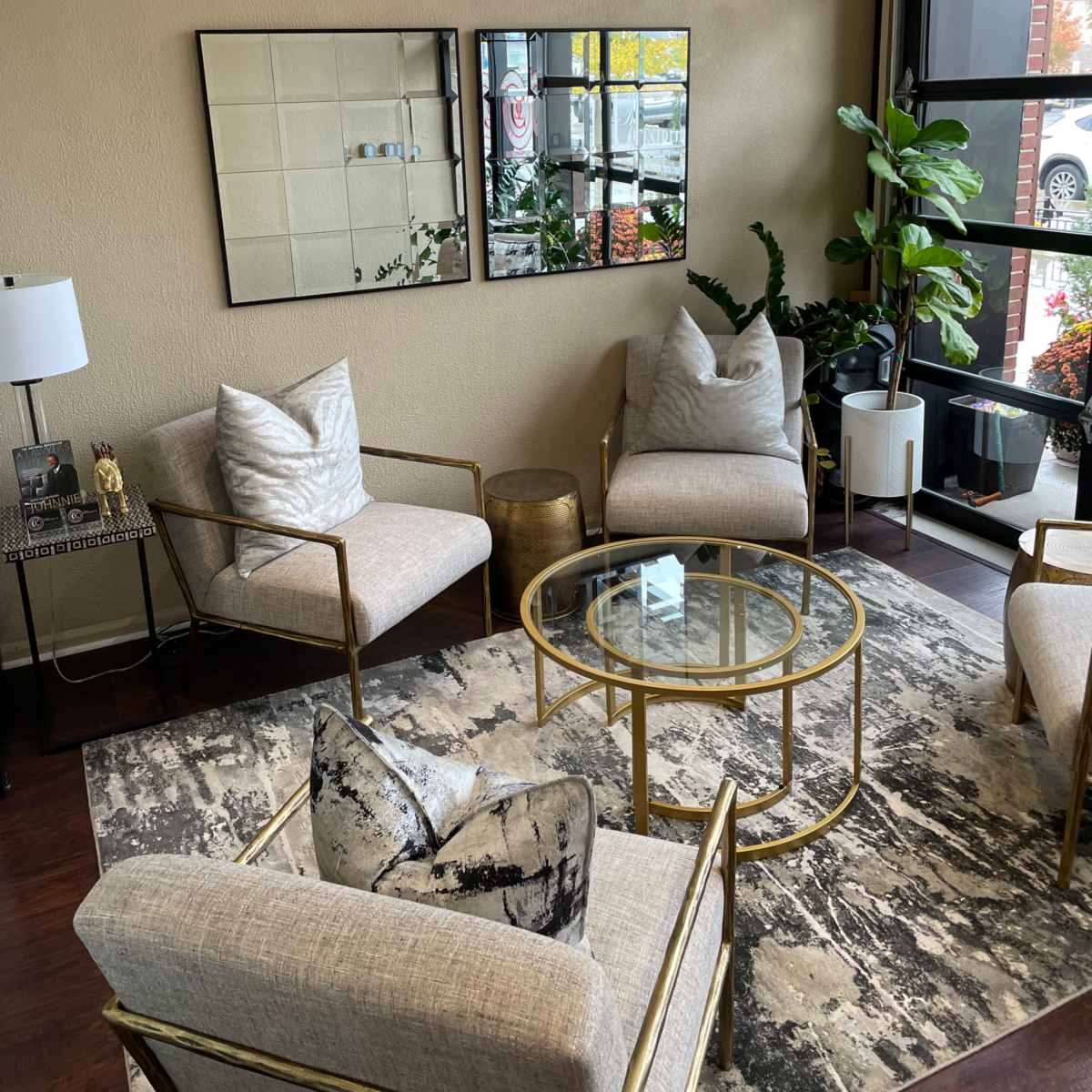 A cozy lounge area featuring four modern chairs, a glass coffee table, and two mirrors on the wall, with plants and decorative items adding to the decor.