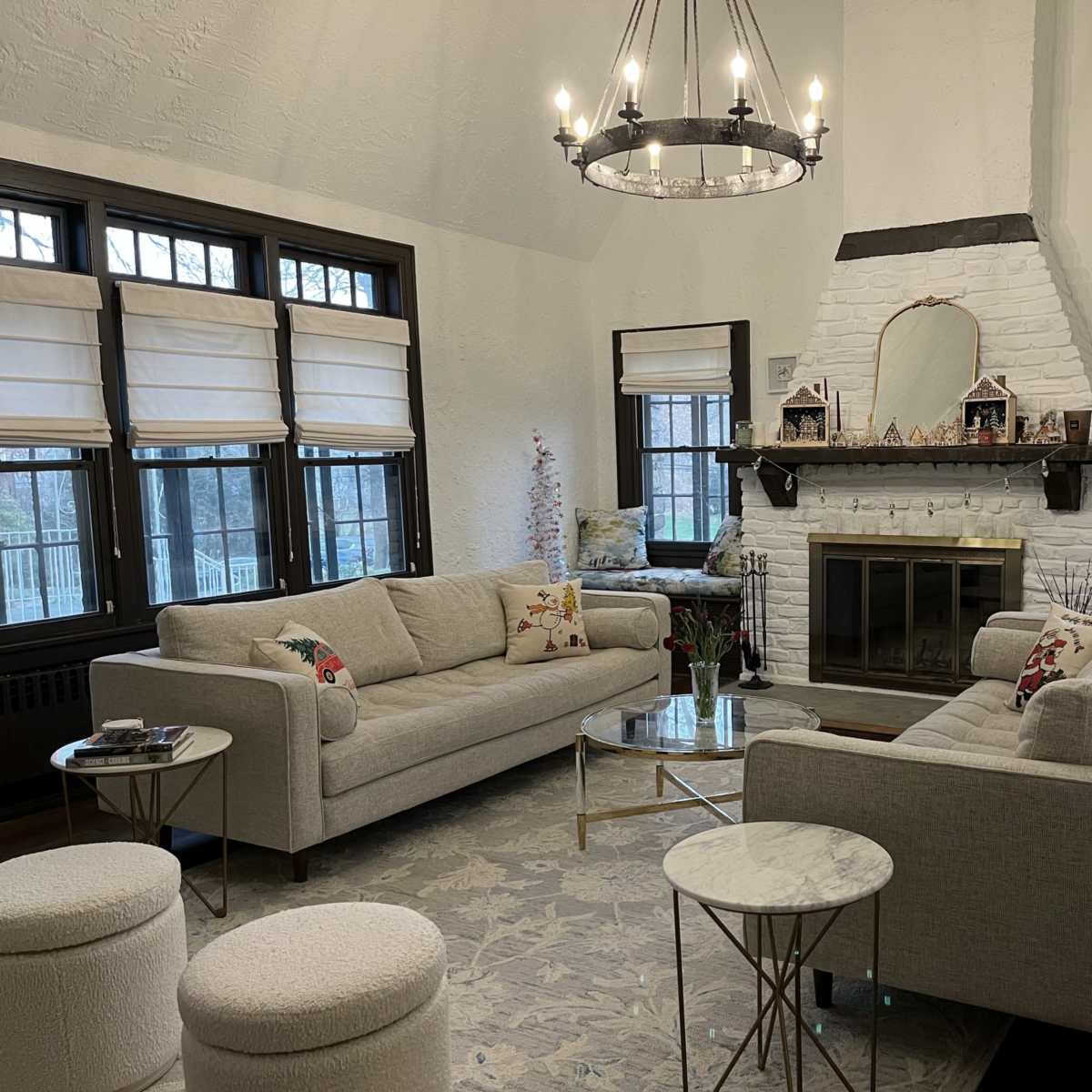 A cozy living room with two sofas facing each other, a fireplace in the center adorned with decorative items, and large windows letting in natural light.