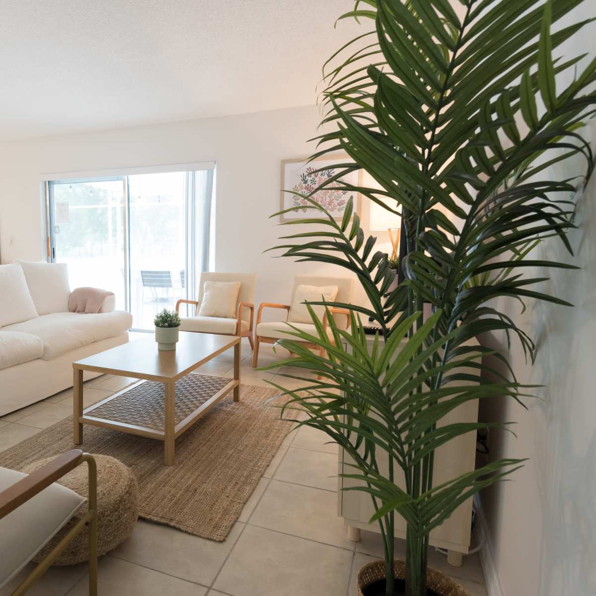 A modern living room with a white sectional sofa, a wooden coffee table on a woven rug, and large windows providing natural light.