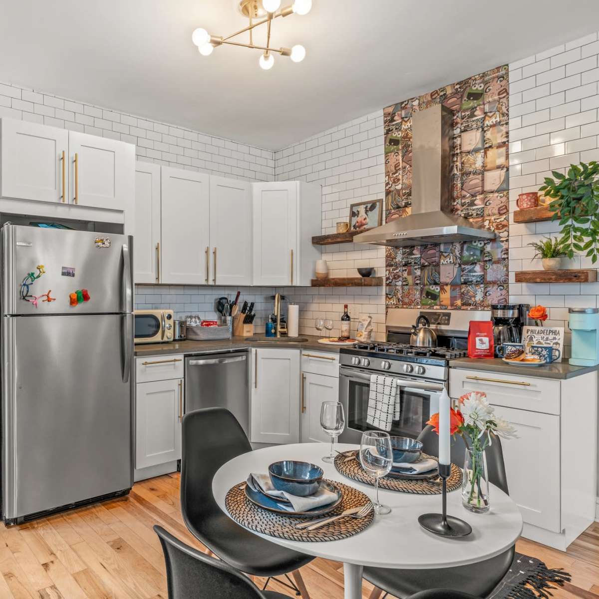 A modern kitchen featuring stainless steel appliances, white cabinetry, and a round dining table set for two.