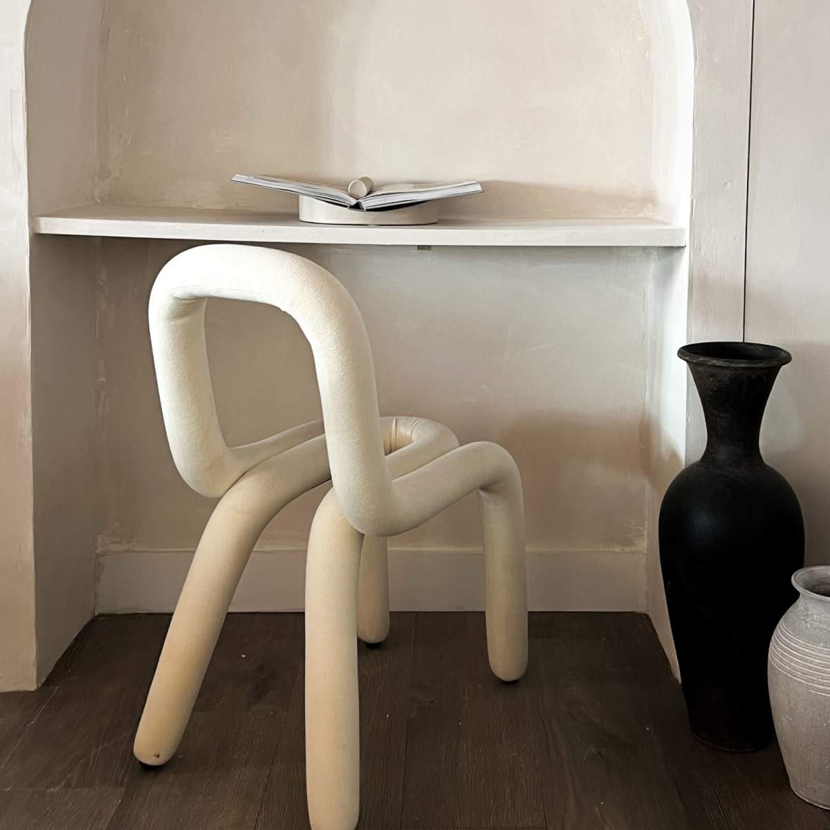 A minimalistic workspace features a white chair and a small table with an open book, set against a softly curved wall.