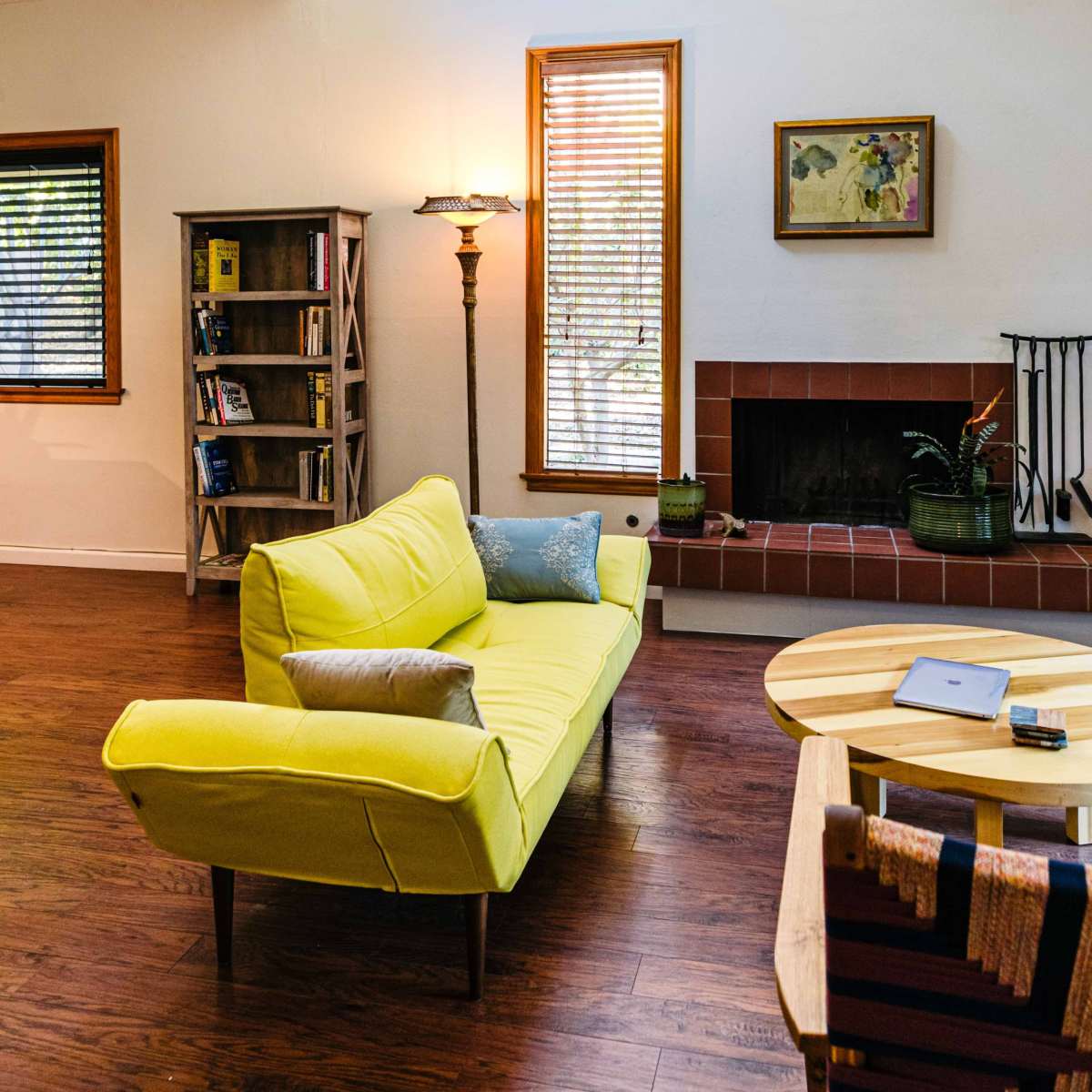 A bright living room features a yellow sofa, a wooden coffee table, a bookshelf, and a fireplace with natural light streaming through a skylight.
