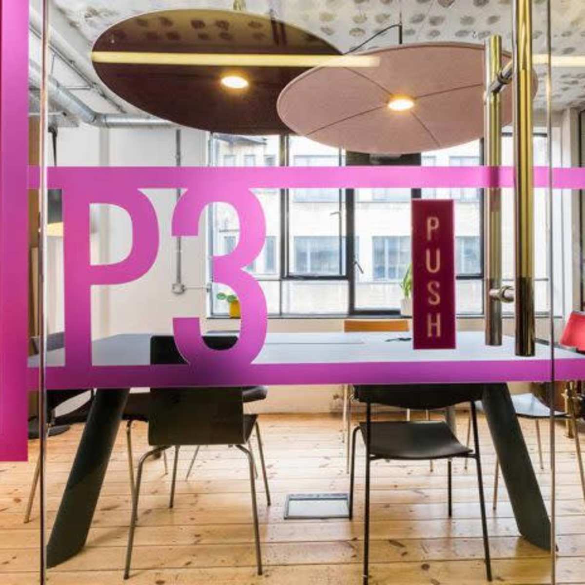 A modern conference room features a glass wall with the letters "P3" and the word "PUSH" displayed, along with a large table and red chairs.