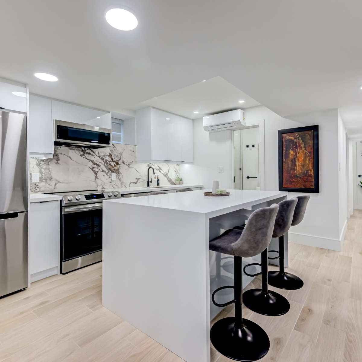 A modern kitchen featuring white cabinetry, a marble backsplash, stainless steel appliances, and a central island with barstools.